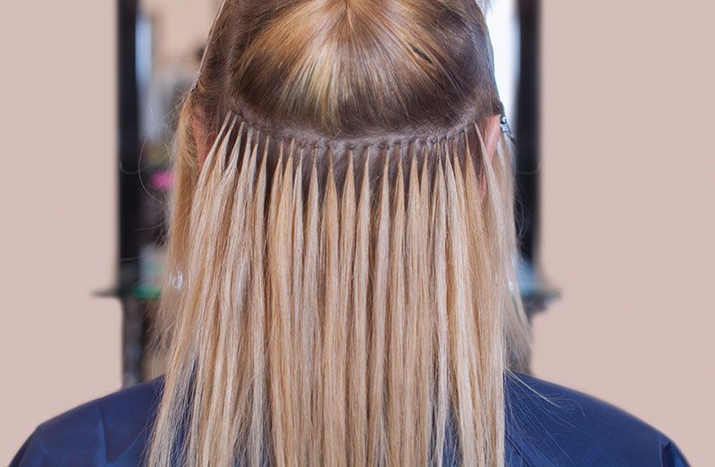 Blonde hair extensions attached to natural hair, seen from the back.