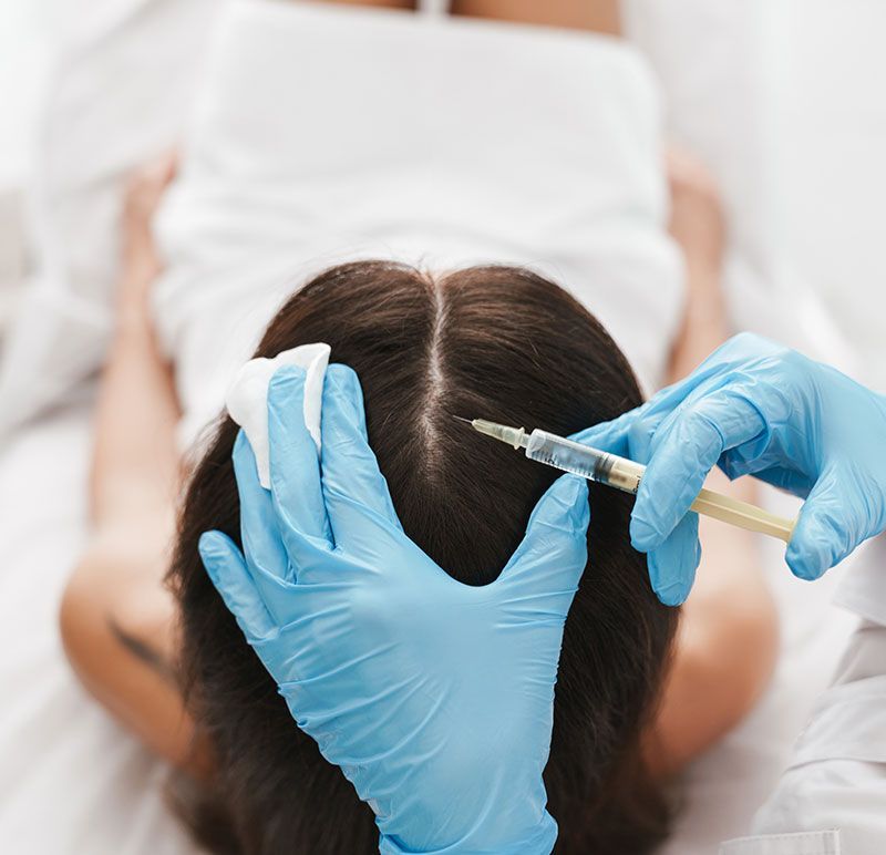 Woman receiving body contouring treatment with a machine on her abdomen. Practitioner wears blue gloves.
