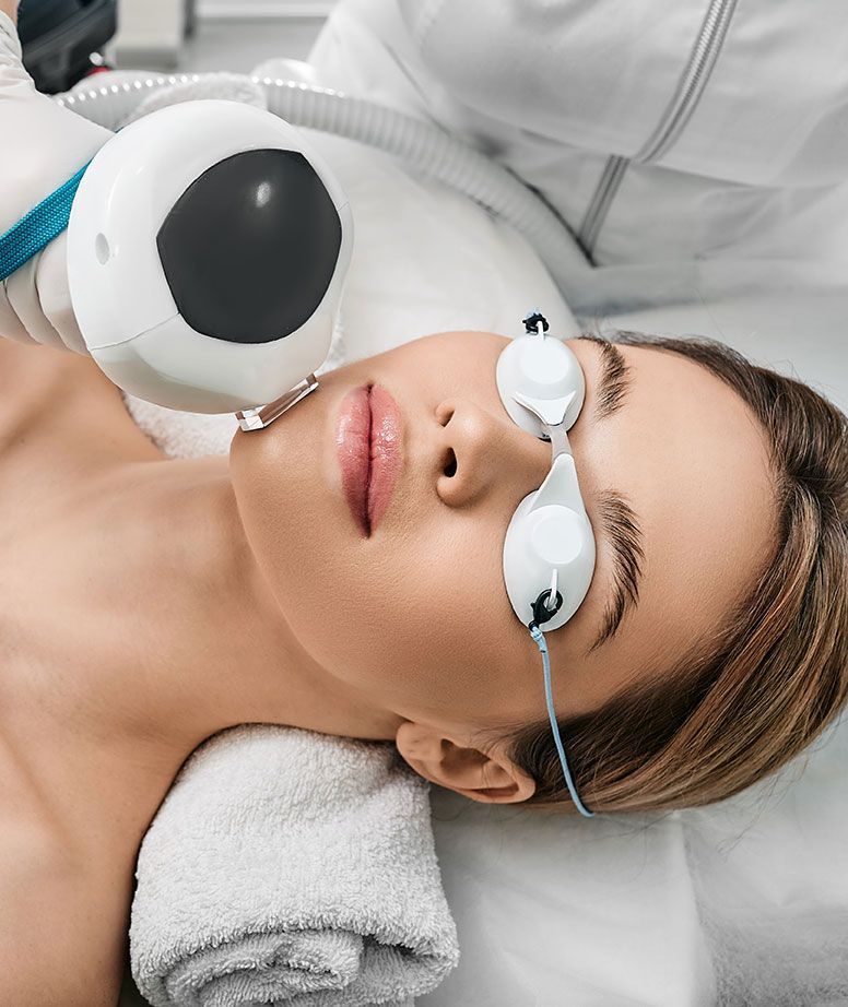 Woman undergoing laser eye treatment, wearing protective goggles; technician holds a light shield.