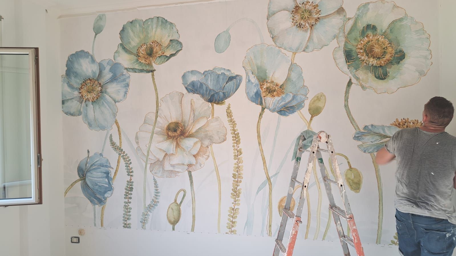 Un uomo è in piedi su una scala e dipinge fiori su un muro.