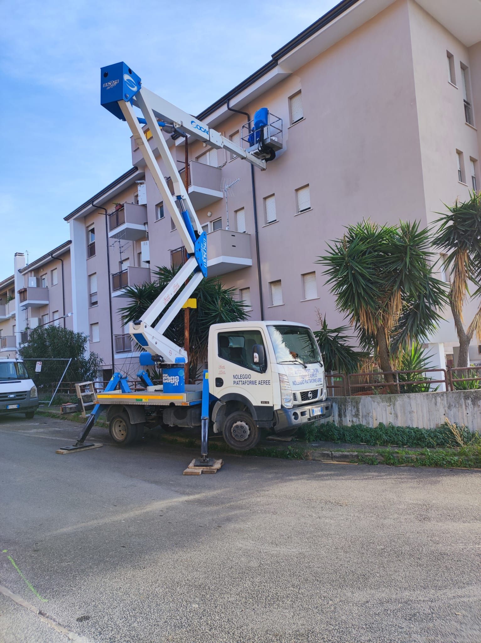 Davanti a un edificio è parcheggiato un camion con sopra una gru.