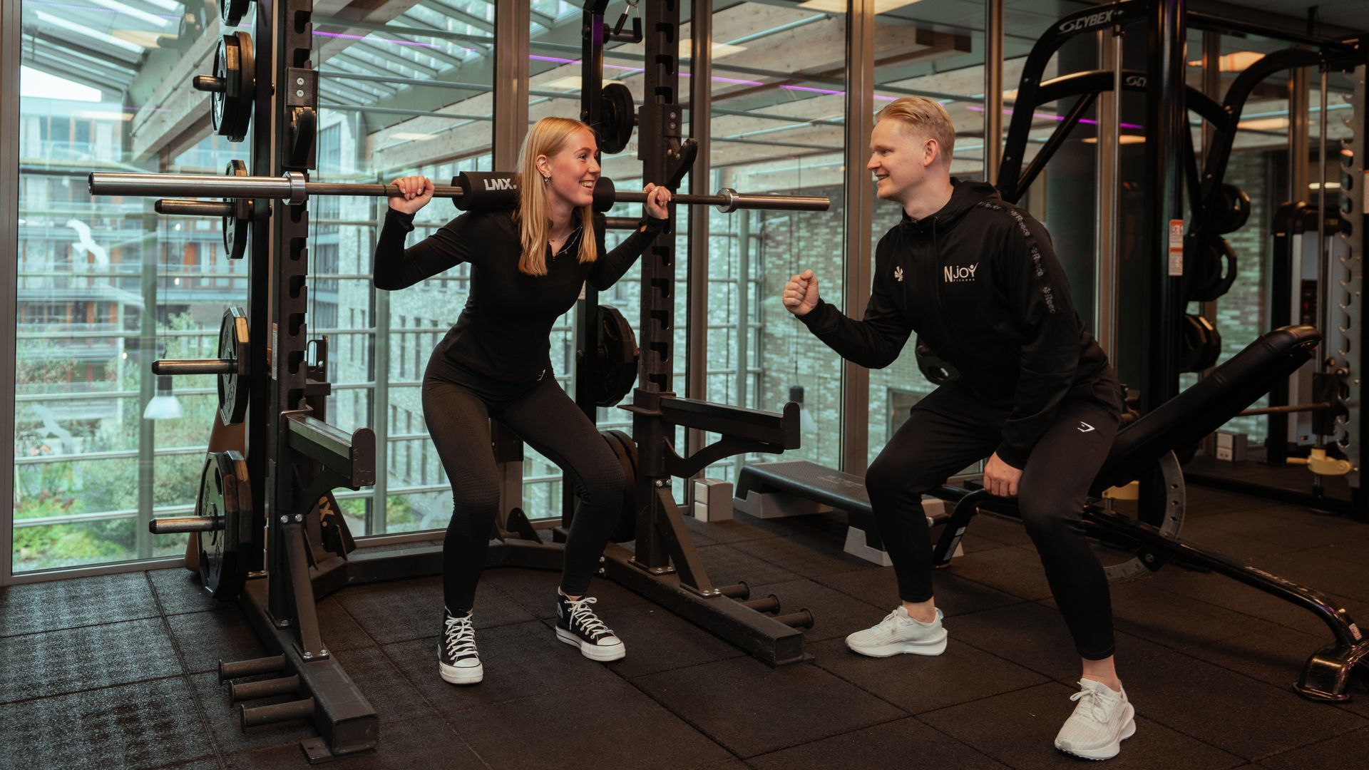 Een man helpt een vrouw met het gebruiken van een apparaat in een sportschool.