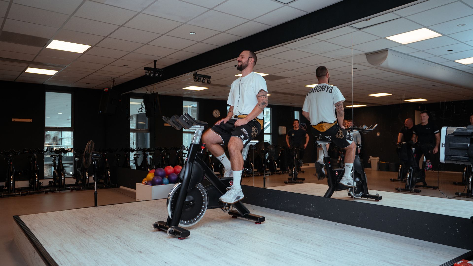 Een man en een vrouw fietsen op een hometrainer in een sportschool.