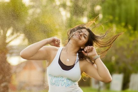 Femme dansant en plein air en débardeur Zumba blanc ; bras levés, cheveux au vent.