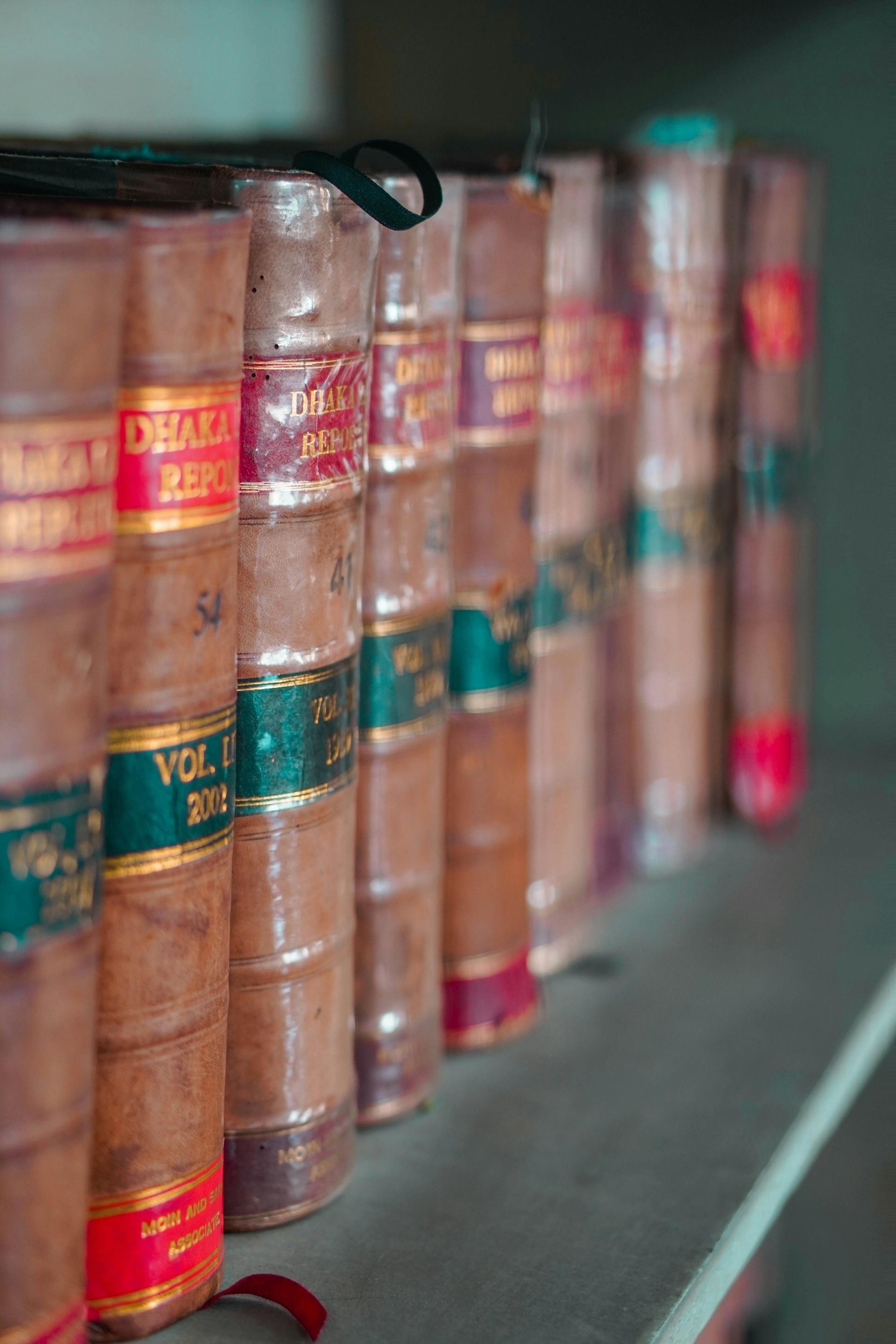 Des livres sur une étagère, des dos reliés en cuir avec des étiquettes et des rubans colorés.
