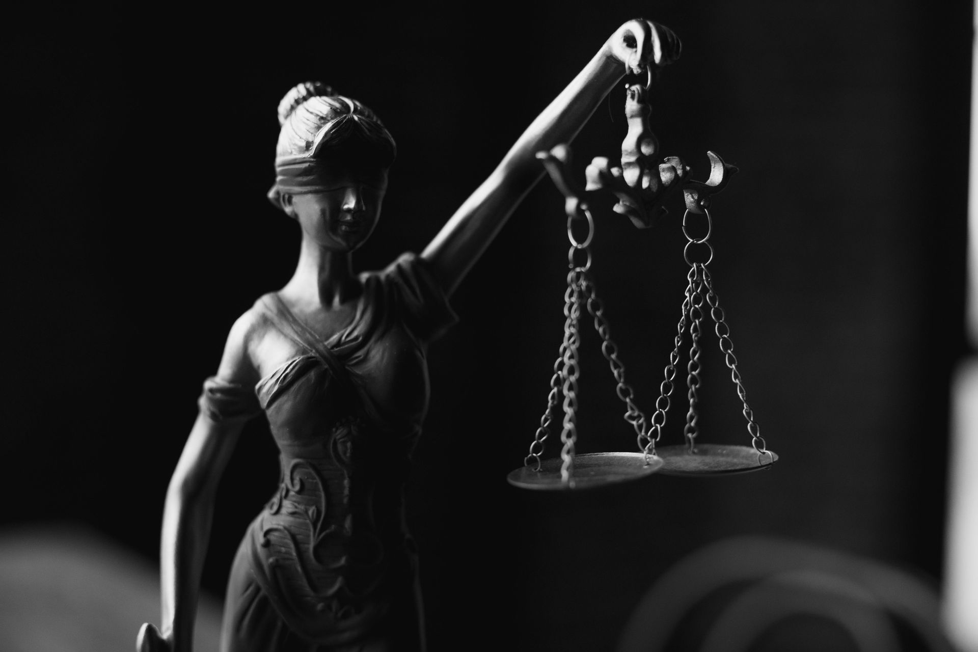 Statue de Dame Justice avec une balance dans la main levée, fond sombre.