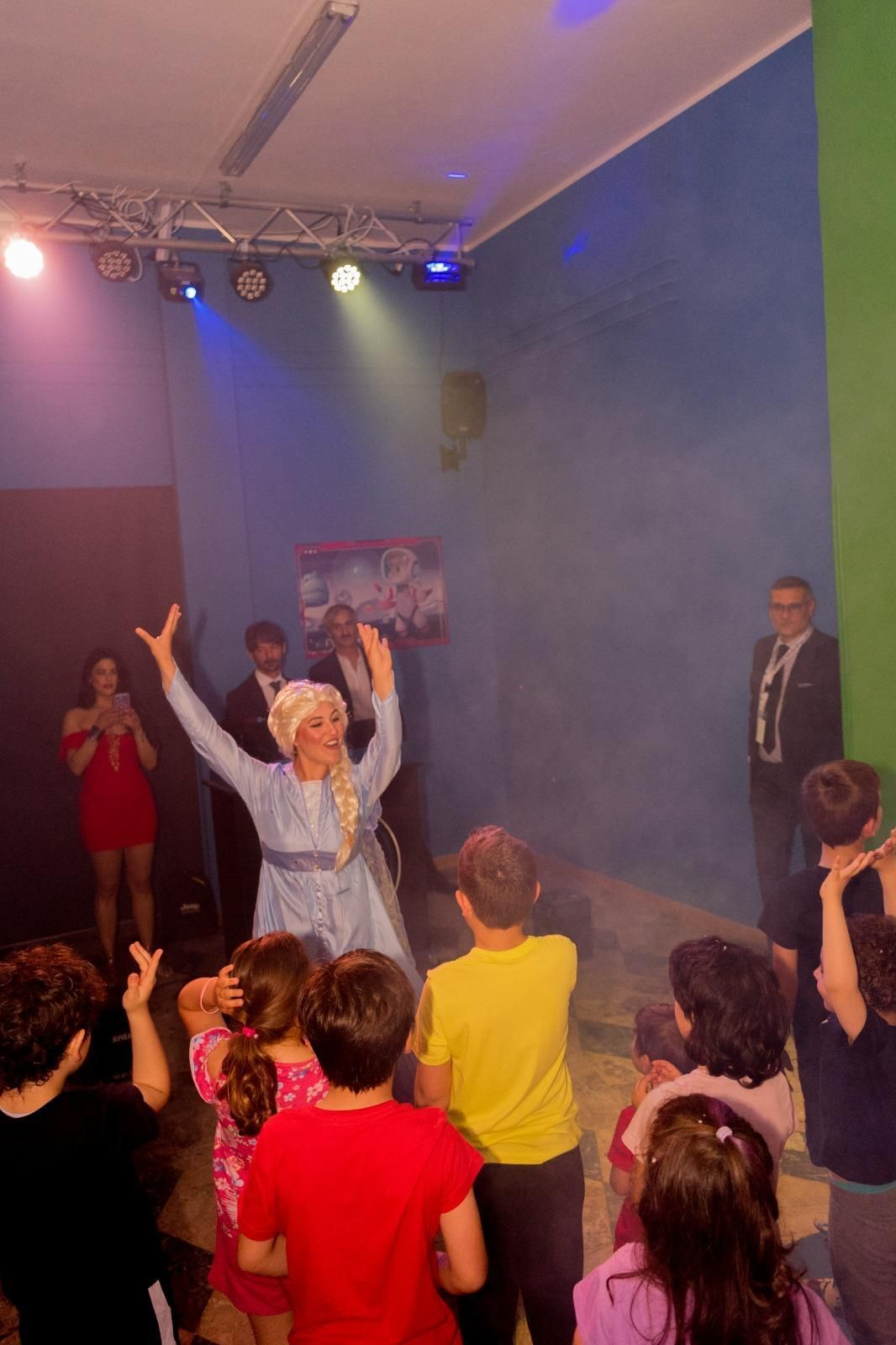 Un gruppo di bambini balla in una stanza con una donna vestita da Elsa di Frozen.