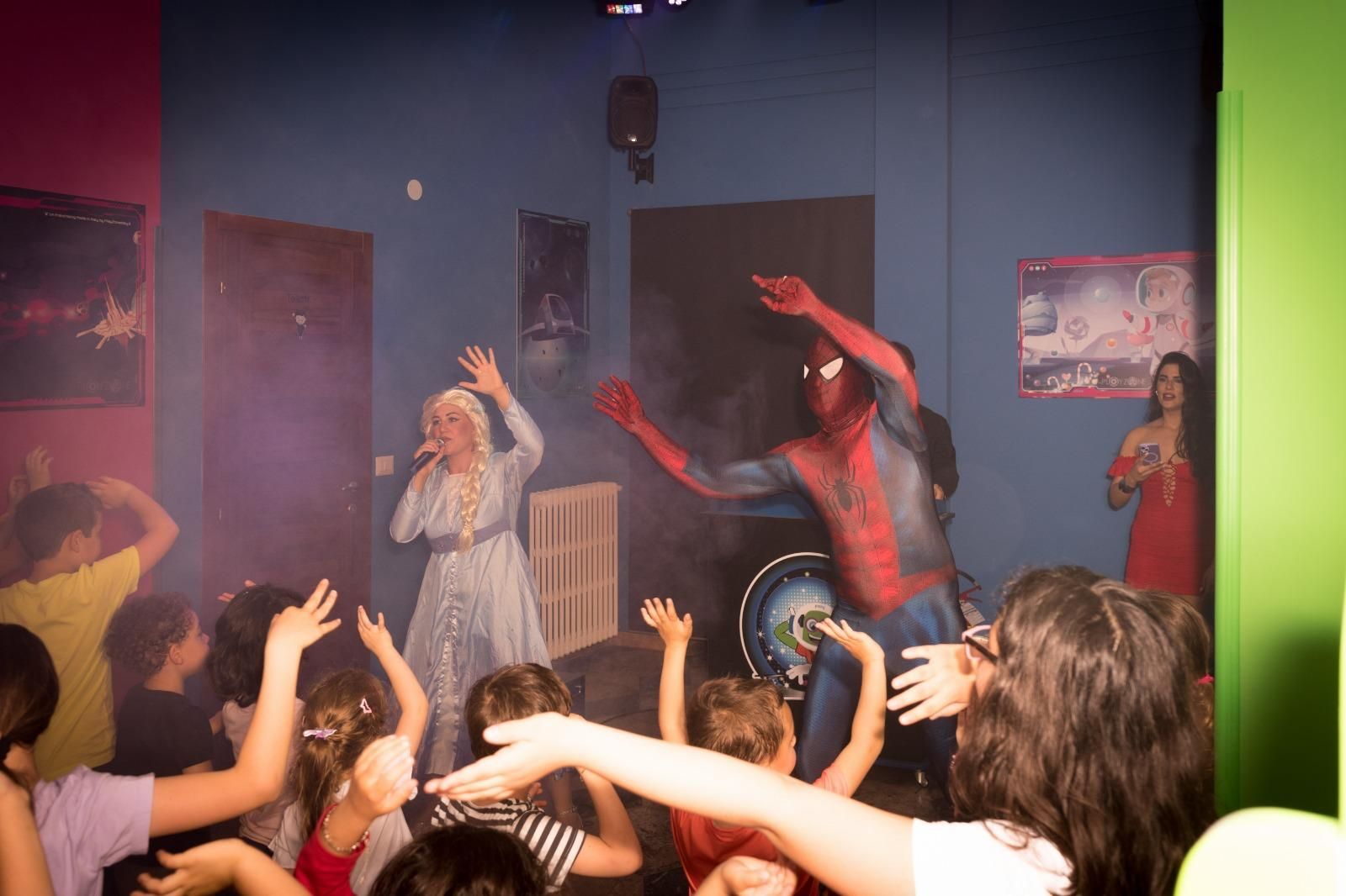 Un gruppo di bambini balla in una stanza con un uomo in costume da Spiderman sul palco.