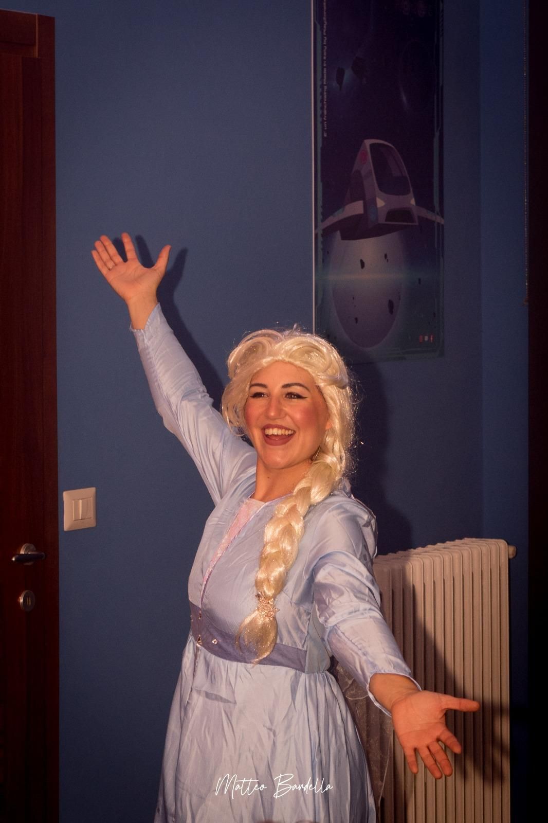 Una donna vestita da elsa di Frozen è in piedi in una stanza con le braccia tese.