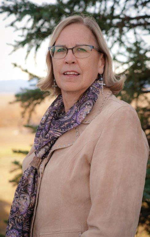 A woman wearing glasses and a scarf is standing in front of a tree.