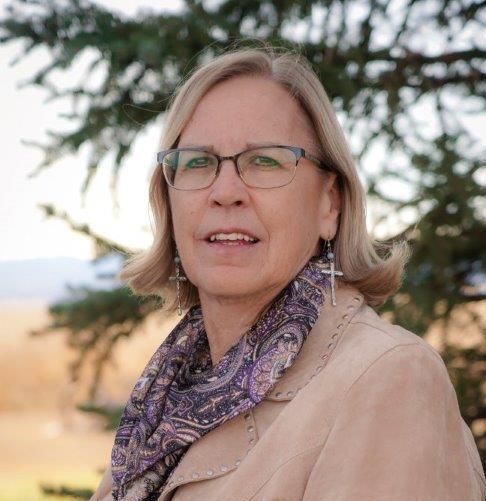 A woman wearing glasses and a scarf is standing in front of a tree.