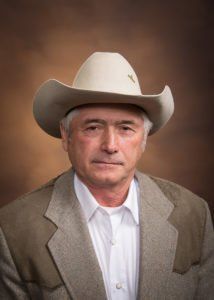A man wearing a cowboy hat and a suit is looking at the camera.