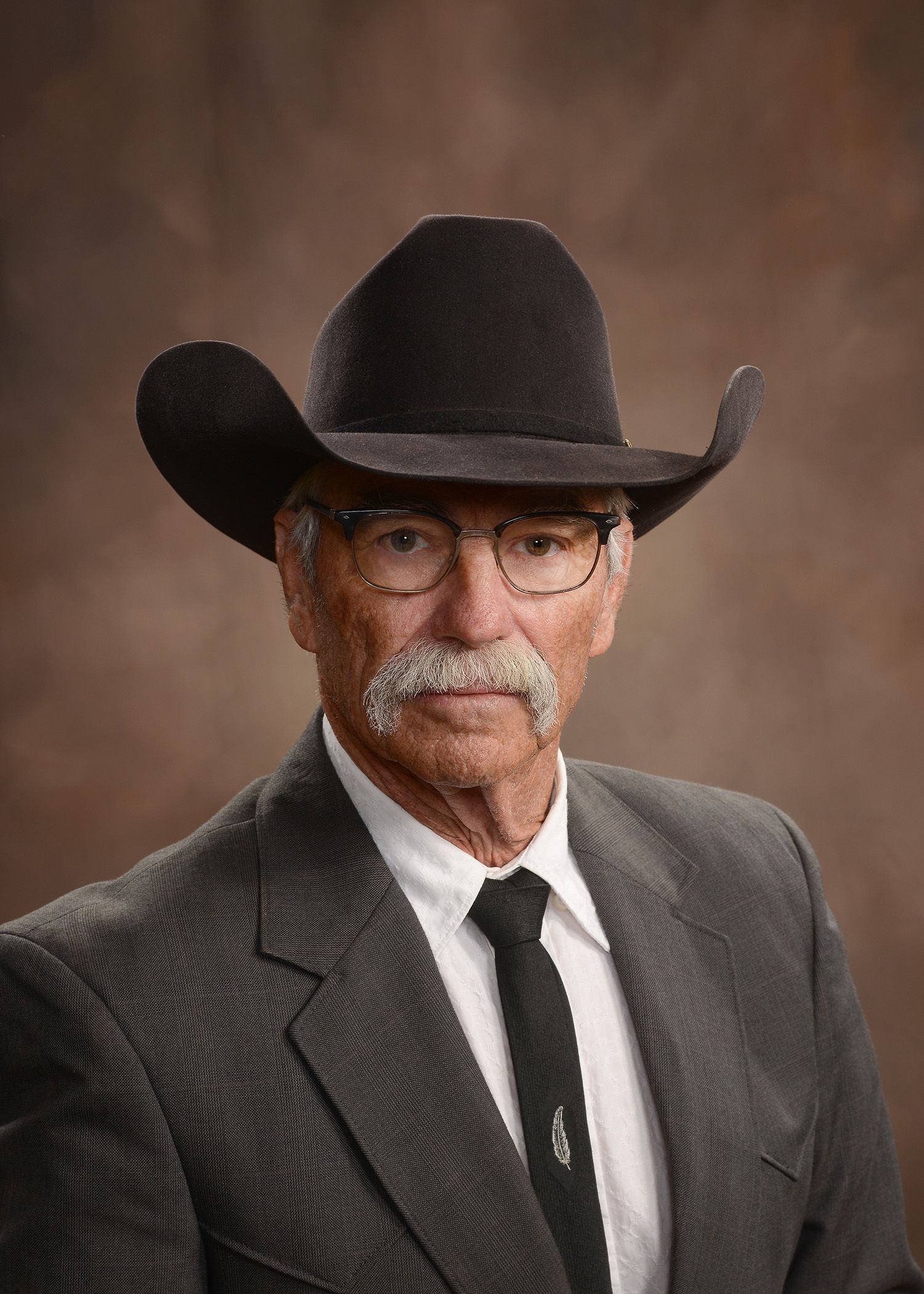 A man in a suit and tie is wearing a cowboy hat and glasses.