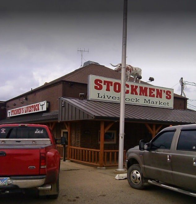 A red truck is parked in front of a stockmen 's livestock market