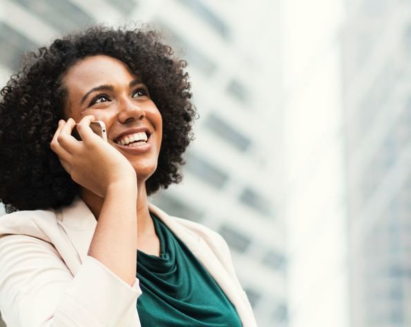 A woman is smiling while talking on a cell phone.