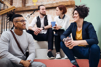 A group of people are sitting on the stairs talking to each other.