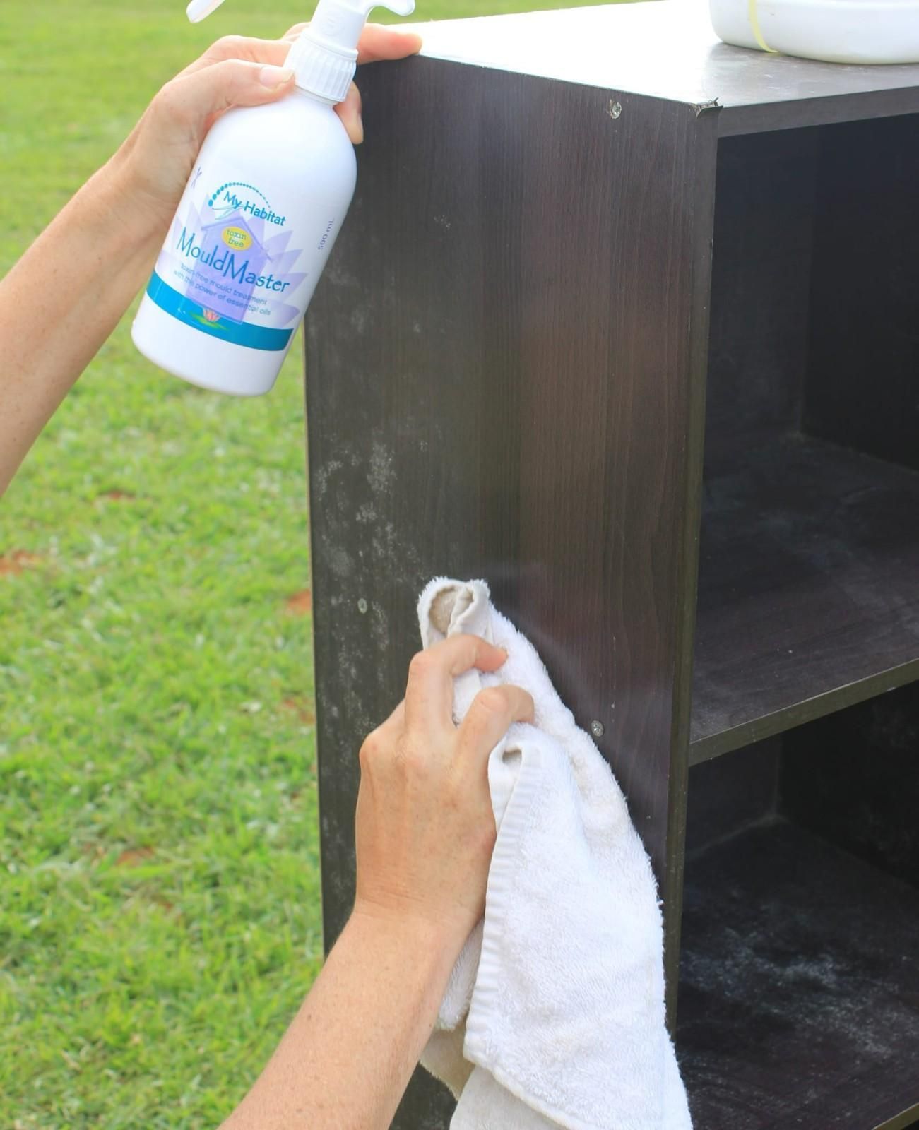 A Person Cleaning a Dark-Coloured Shelf Unit Outdoors with Spray and A White Cloth — My Habitat Products in Malanda, QLD