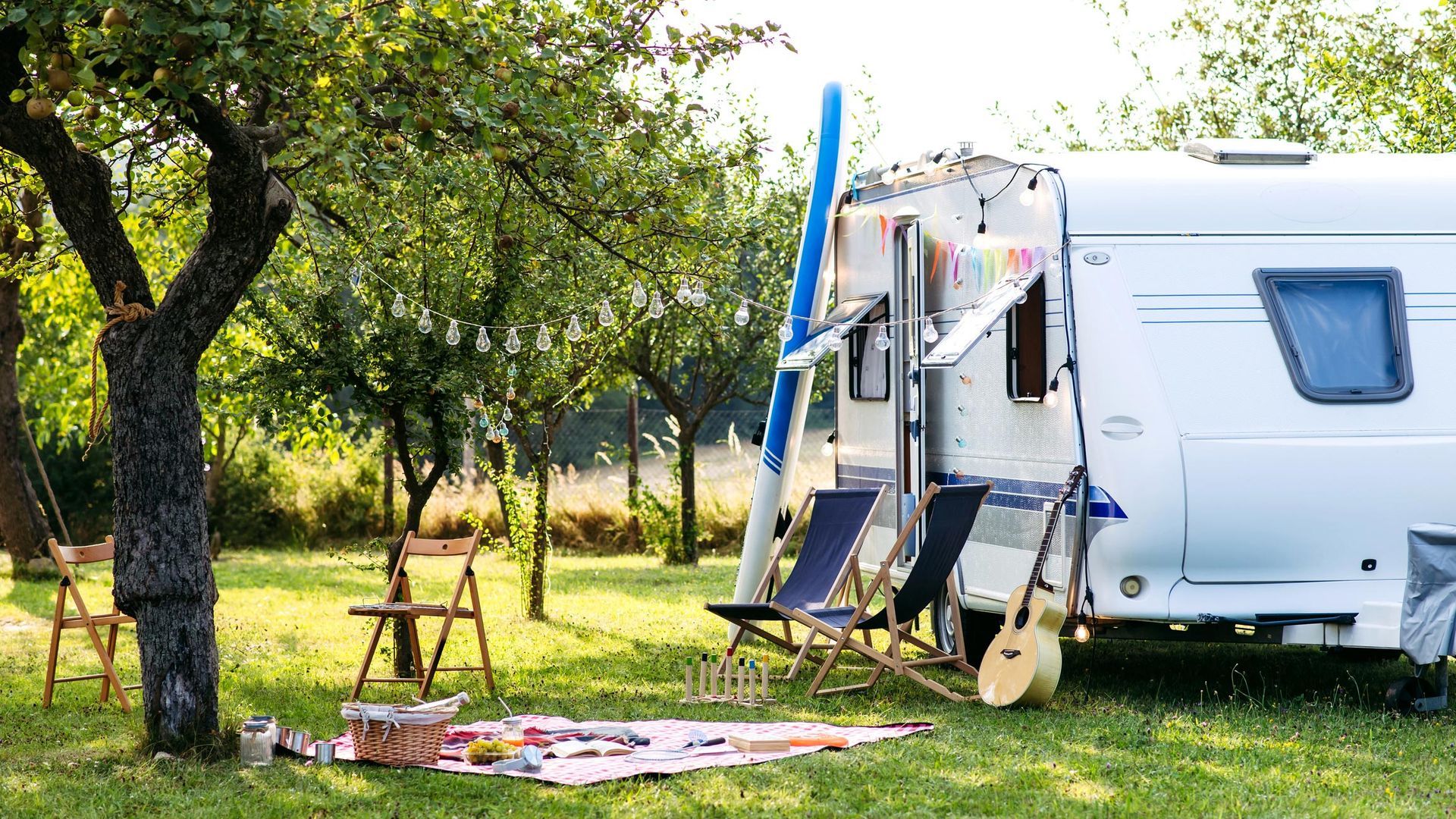 A camper is parked in a grassy field with chairs and a guitar.