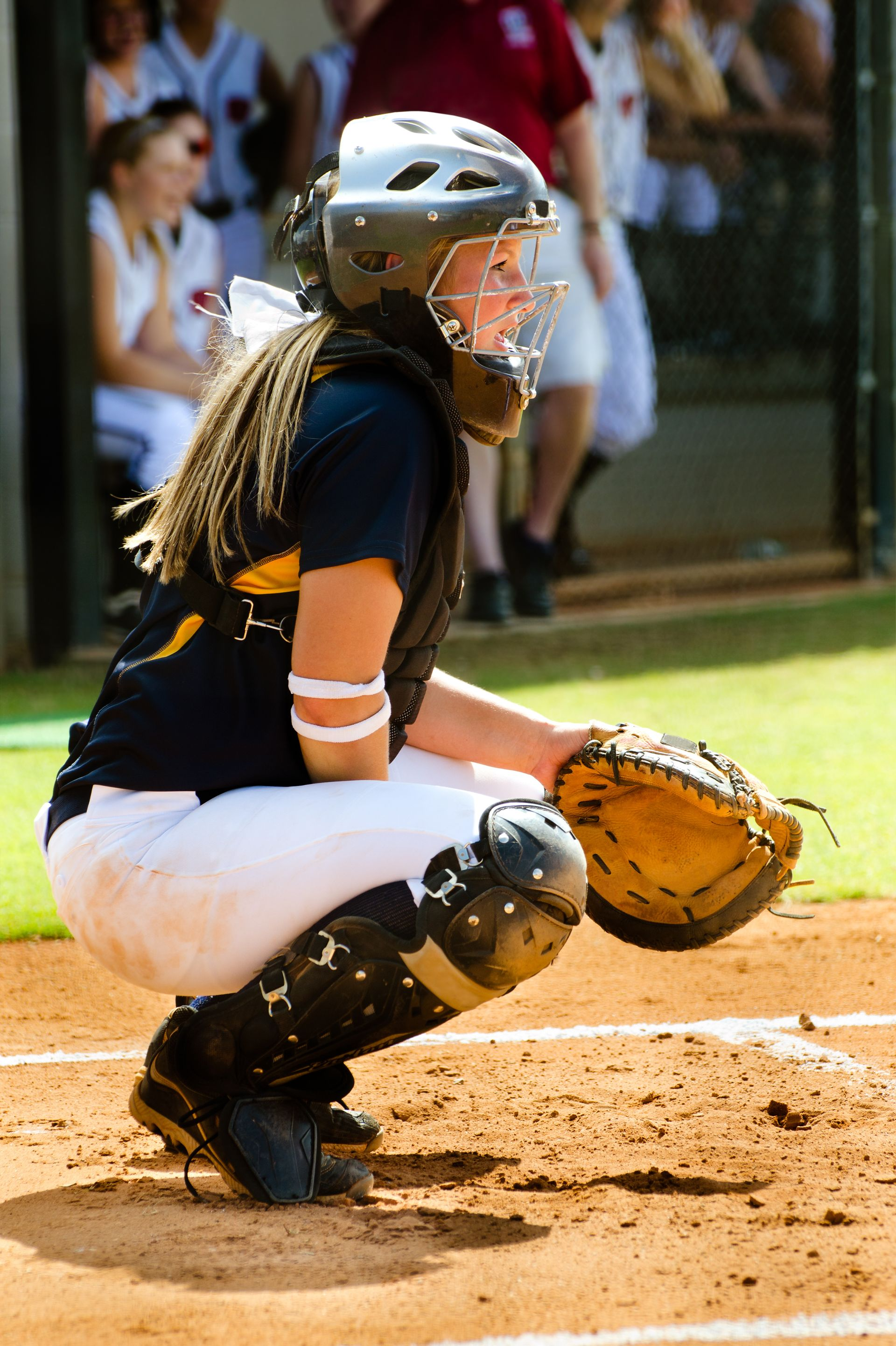A person wearing a hat and orange shirt, holding a baseball bat on their shoulder on a baseball field.