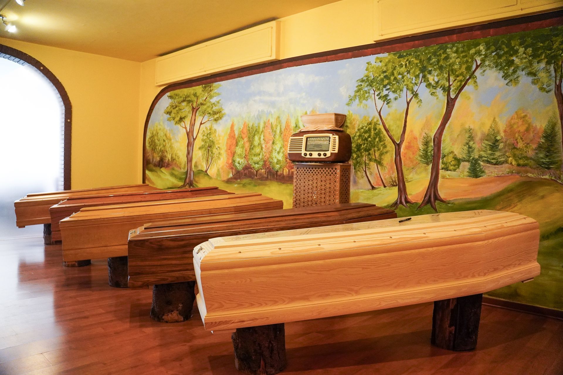 Una stanza piena di bare di legno e un dipinto sul muro.