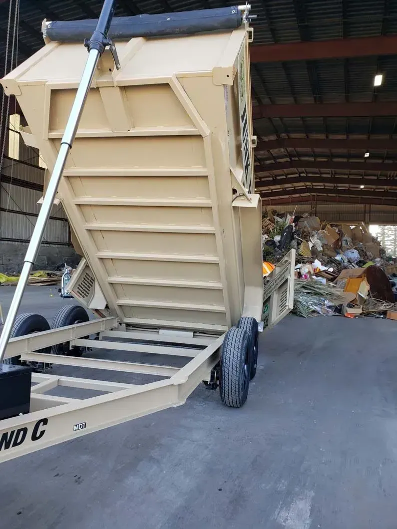 A dumpster trailer is parked in front of a pile of trash.