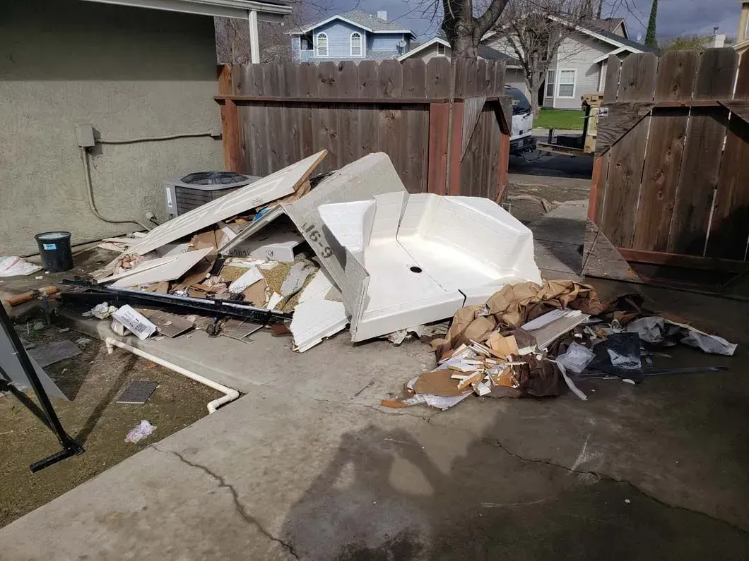 A pile of trash is sitting on the ground in front of a wooden fence.