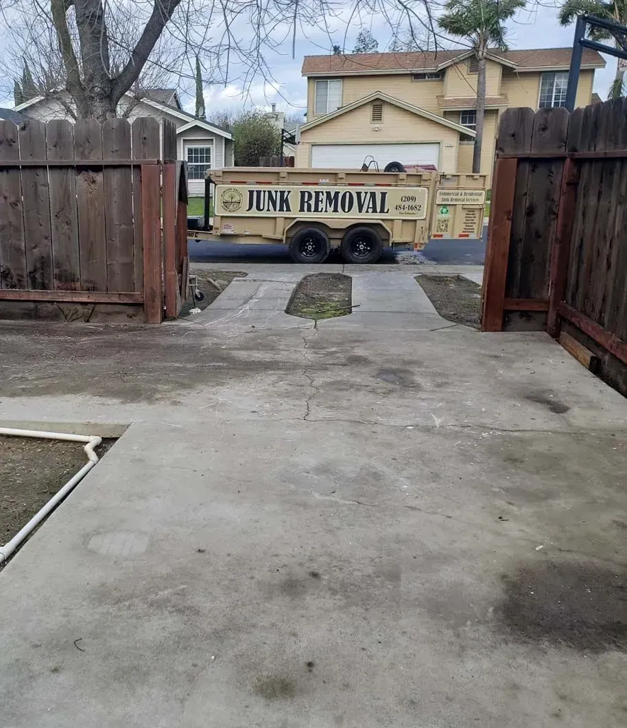 A junk removal truck is parked in a driveway next to a wooden fence.