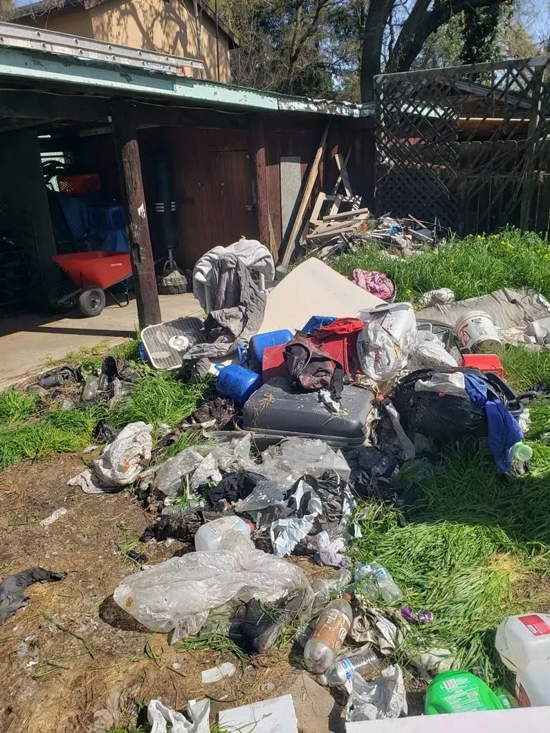A pile of trash is sitting in the grass in front of a garage.