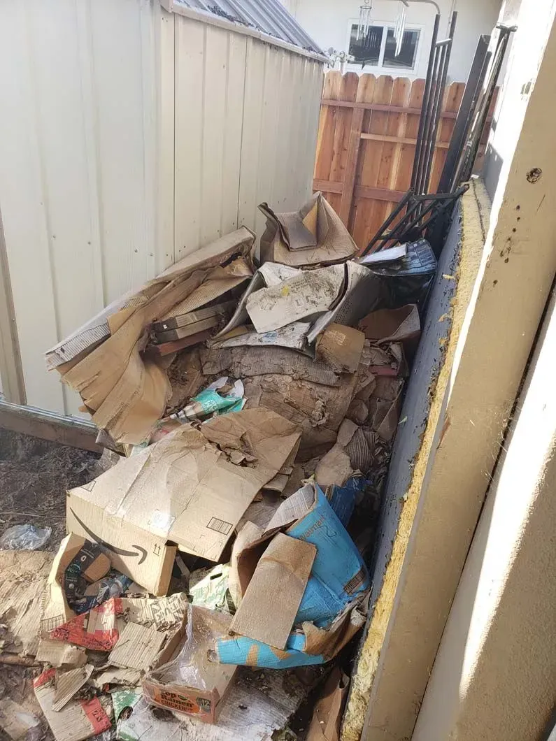 A pile of cardboard boxes and trash is sitting in a backyard next to a fence.