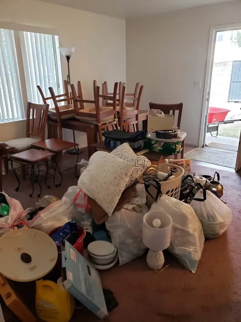 A living room filled with lots of junk and a table and chairs.