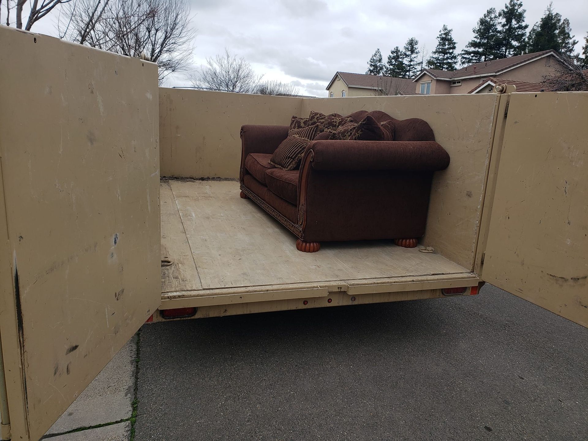 A brown couch is in the back of a dumpster