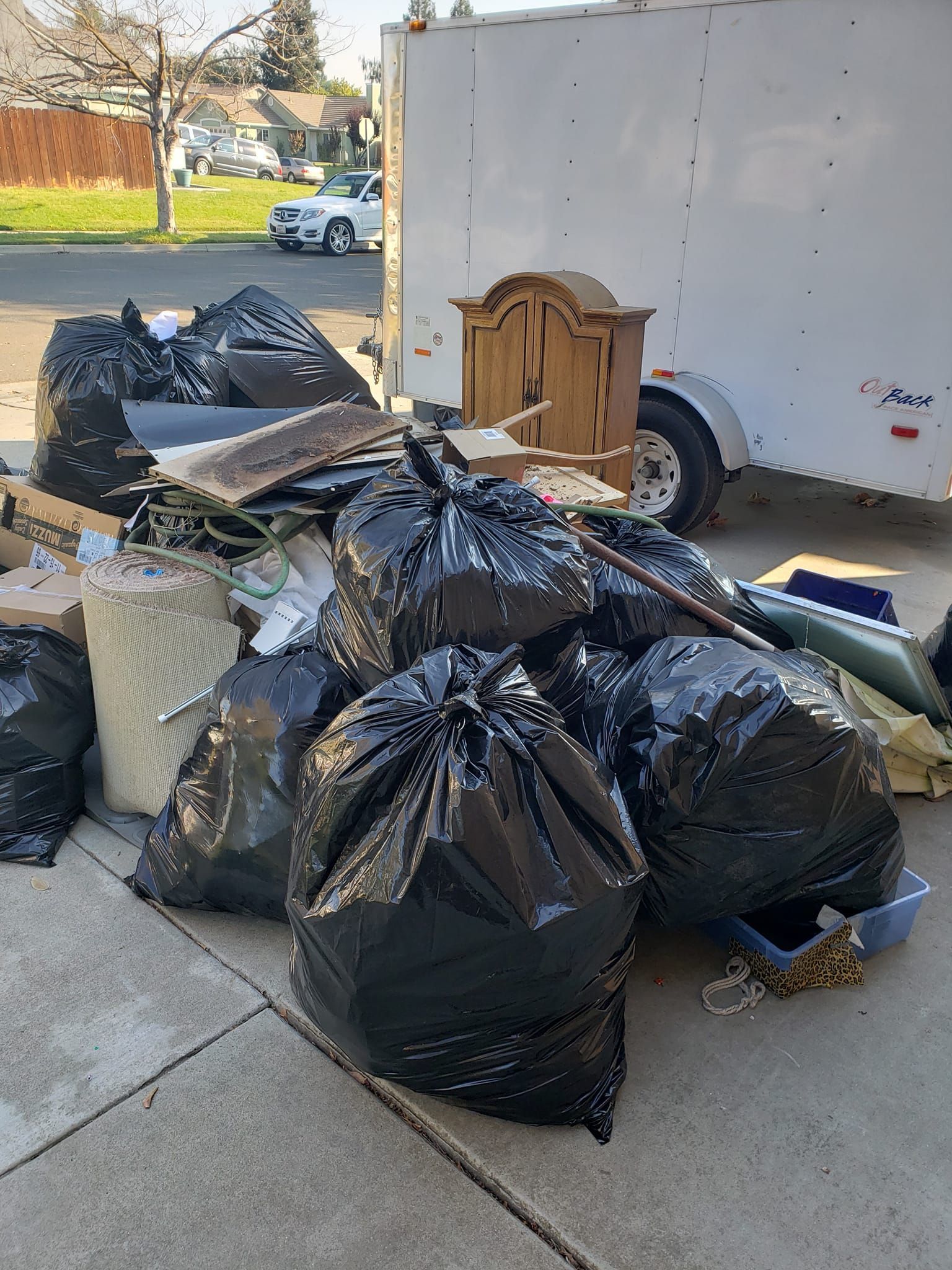 A pile of trash bags is sitting on the sidewalk in front of a trailer.