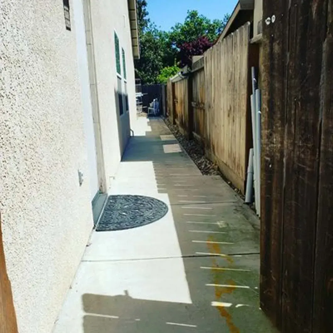 A narrow walkway between two houses with a wooden fence