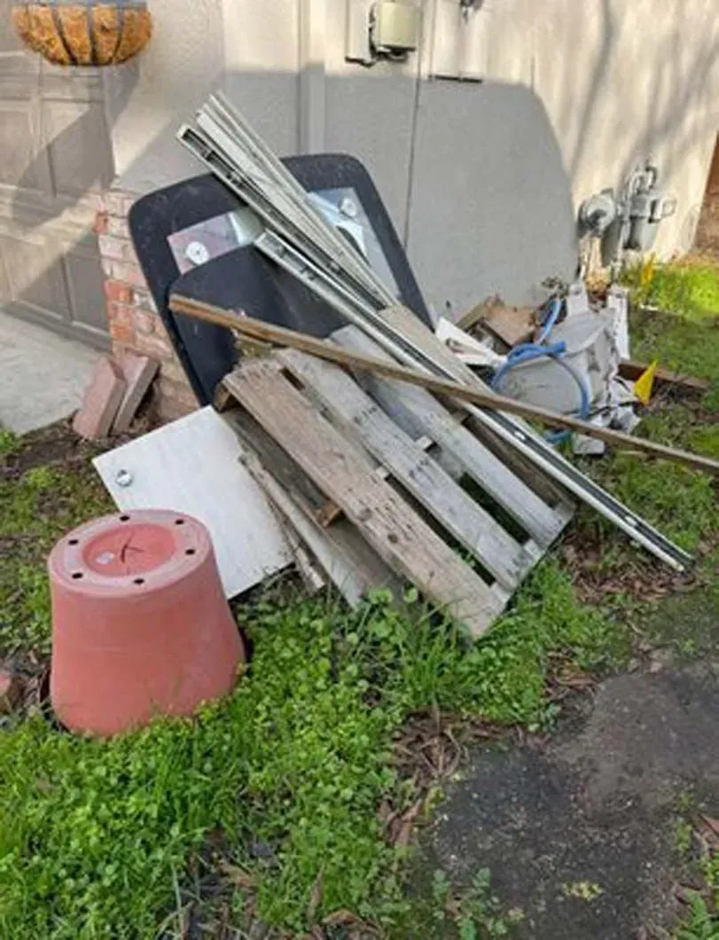A pile of trash is sitting in the grass in front of a house.