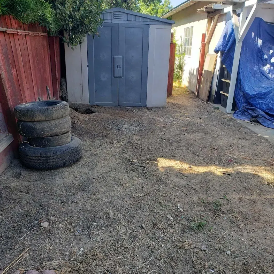 A stack of tires sits in the dirt in front of a shed.