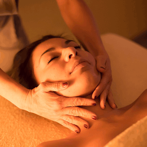 Donna che esegue un massaggio alla schiena in una stanza scarsamente illuminata, con candele e fiori.