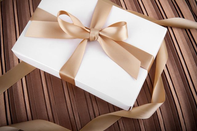 Scatola regalo bianca con nastro dorato su superficie marrone a strisce.