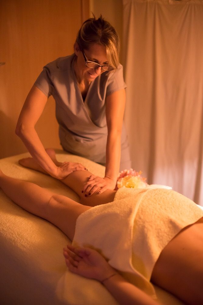 Massaggiatrice che esegue un massaggio alle gambe in una stanza scarsamente illuminata; il cliente è sdraiato a faccia in giù su un lettino da massaggio.