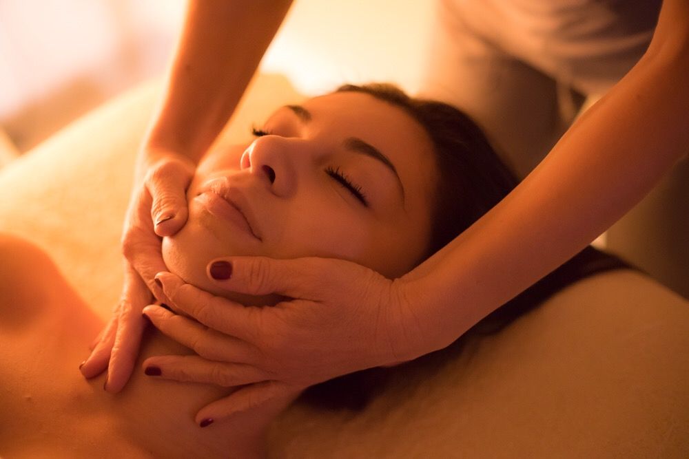 Donna che riceve un massaggio facciale con le mani sul viso e sul collo, occhi chiusi.