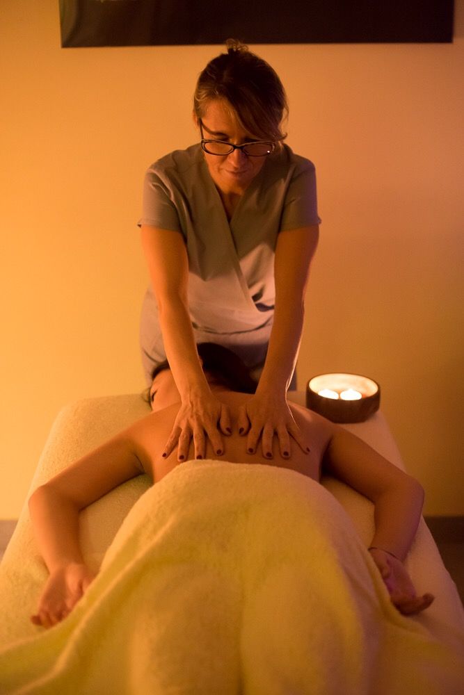 Massaggiatrice che esegue un massaggio alla schiena; luce calda, asciugamano sul cliente.