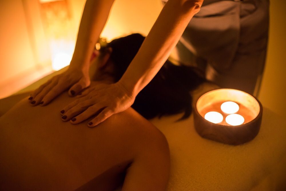 Una persona riceve un massaggio da seduta. Un terapista in camice grigio massaggia la schiena del cliente. Tappeto rosso, stanza scarsamente illuminata.