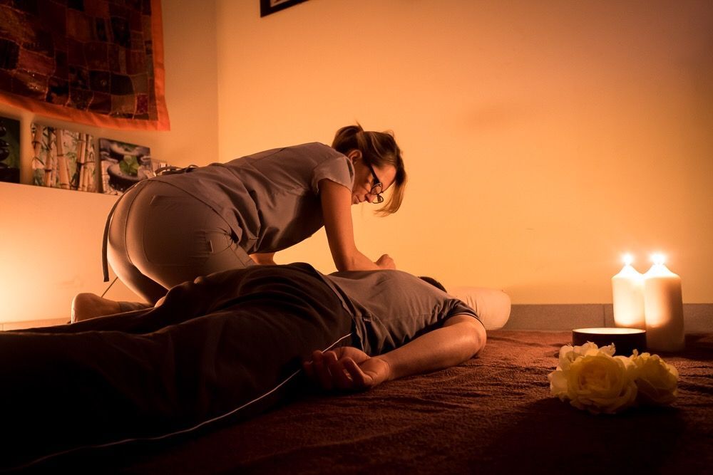 Donna che esegue un massaggio alla schiena in una stanza scarsamente illuminata, con candele e fiori.