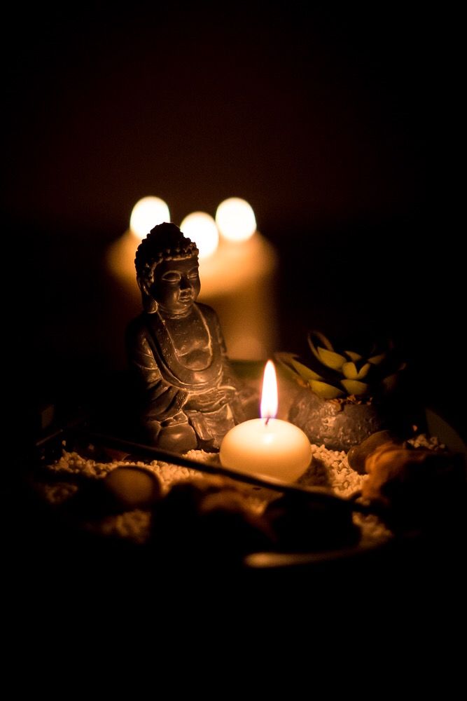 Statua del Buddha con candela accesa, circondata da pietre e luce soffusa in un ambiente buio.
