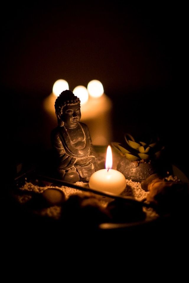 Statua del Buddha con candela accesa, circondata da pietre e luce soffusa in un ambiente buio.