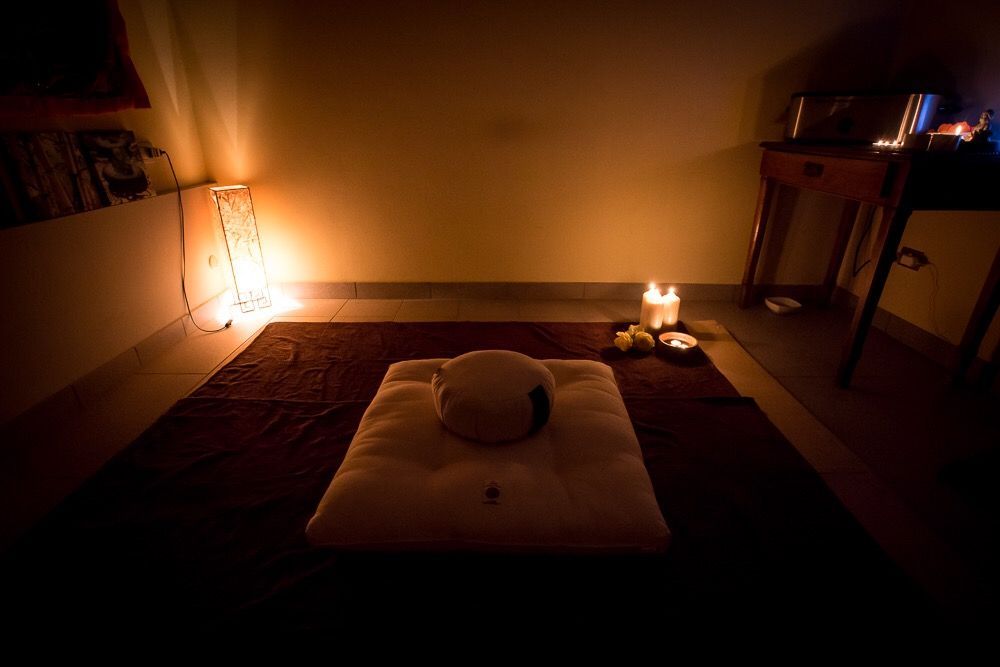 Spazio per la meditazione: cuscino con poggiatesta, candele e luci soffuse in una stanza scarsamente illuminata.