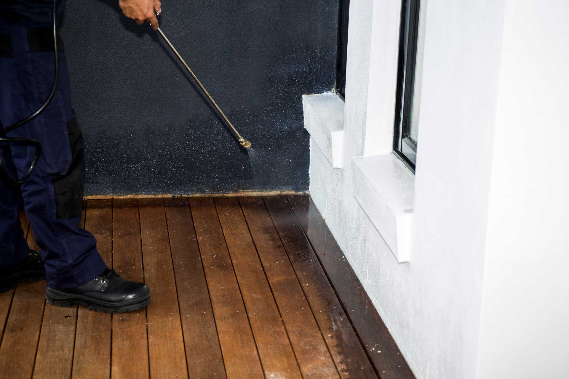 Person spraying pesticide on wooden floor near a white wall and dark door. Person spraying pesticide on wooden floor near a white wall and dark door.