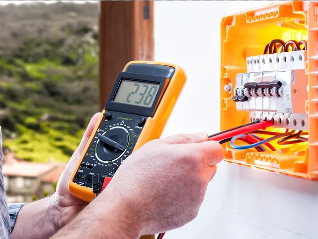 An electrician is using a digital multimeter to test a circuit board.