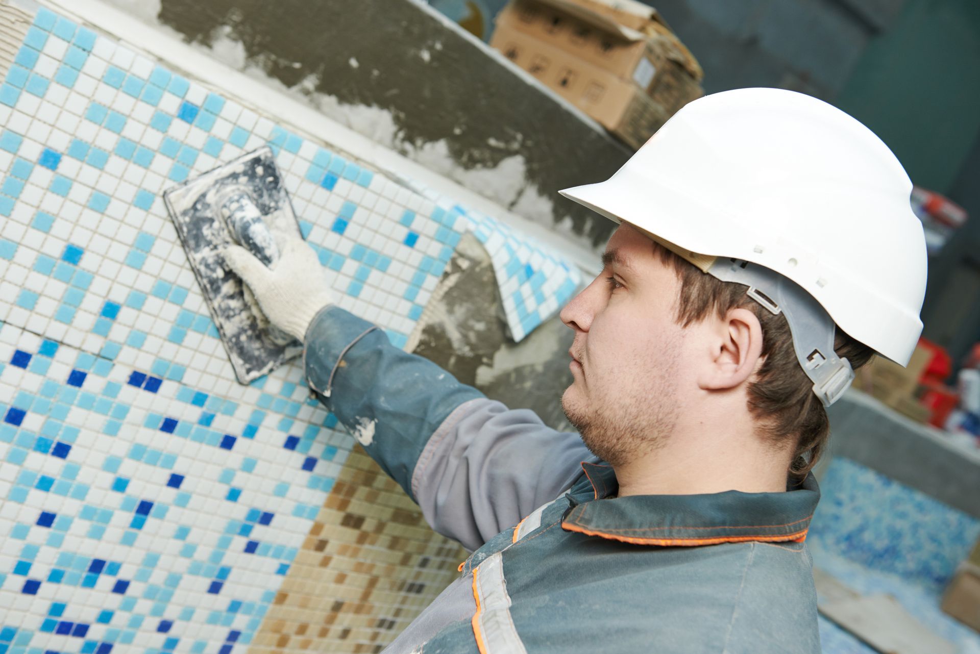 A man wearing a hard hat is working on a tiled wall.