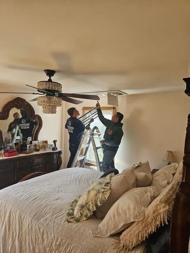 A technician wearing gloves checks an air conditioning unit with a dual-gauge manifold set outdoors.
