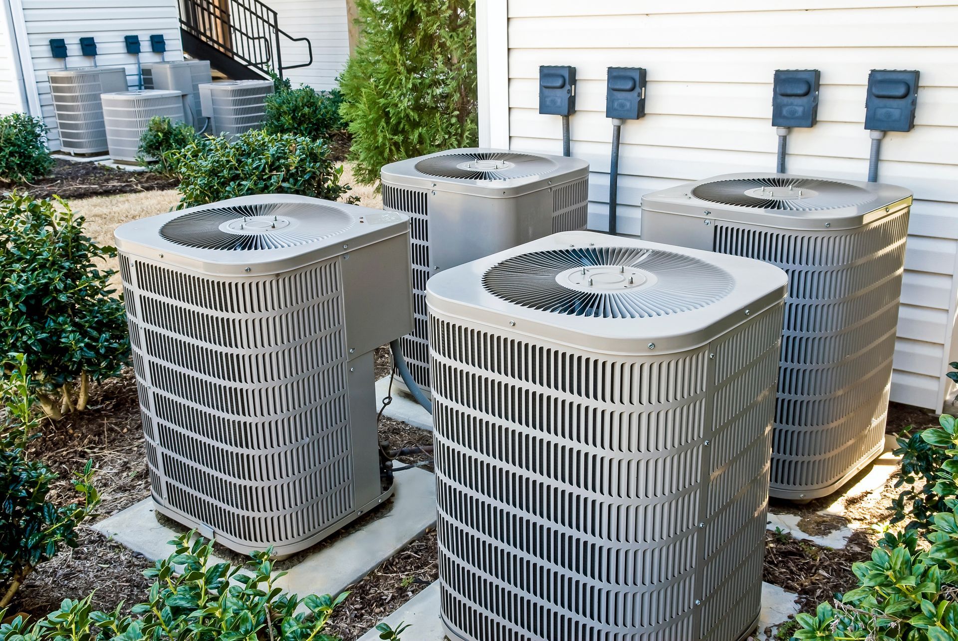 Industrial air conditioning units installed on a flat rooftop against a backdrop of green trees.